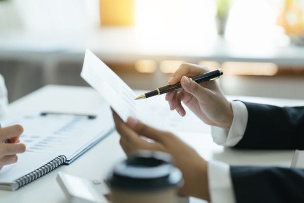Mujer señala con su bolígrafo gráficos que están en la hoja de papel que sostiene .